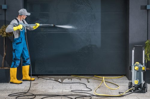 Man using high pressure water to clean his garage door